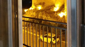 Vista noturna de um edifício com paredes iluminadas e entrada protegida por grades.