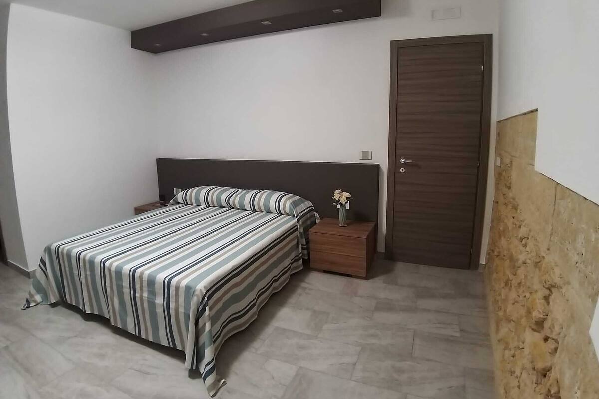 Un dormitorio con cama, mesita de noche, cómoda y puerta.