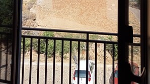 Vista de uma varanda com um edifício de pedra ao fundo, guarda-corpo de metal e um carro estacionado.