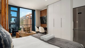 Een moderne hotelkamer met een bed, een bureau, een televisie en uitzicht op de stad.