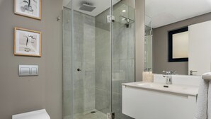 Een moderne badkamer met een douche in een glazen cabine, een witte wastafel en een toilet.
