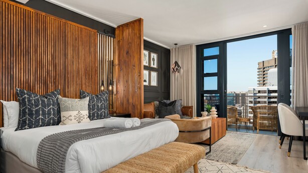 Een moderne slaapkamer met een groot bed, een wand van houten panelen en een uitzicht op de stad door grote ramen.