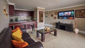 A modern living room with a leather sofa, a glass coffee table, and a kitchen area with dark cabinets and a stainless steel sink. - SEA-VIEW  APARTMENT - POINT WATERFRONT
near to beaches , harbour and restaurants (Durban)