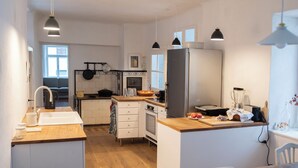 Een moderne keuken met een centraal eiland, witte kasten en een houten aanrecht. Er is een spoelbak, een kookplaat en een koelkast.