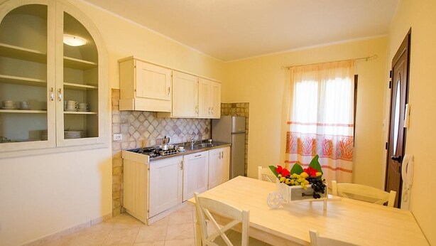 A compact kitchen with white cabinets, a gas stove, and a dining table with chairs. - Relaxing Le Residenze del Maria Rosaria No2227h (Orosei)