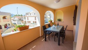 A balcony with a table and chairs, potted plants, and a view of neighboring buildings. - Relaxing Le Residenze del Maria Rosaria No2227h (Orosei)