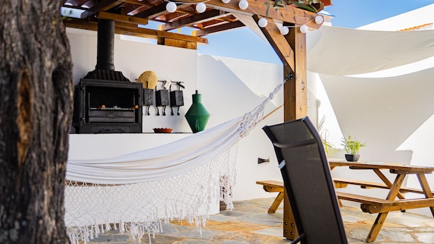 A stone patio with a hammock, a wooden table, and a barbecue grill.