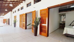A hotel corridor with wooden doors, potted plants, and a bed in one room.