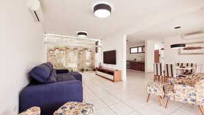 A modern living room with a sofa, TV, and dining area with striped chairs.