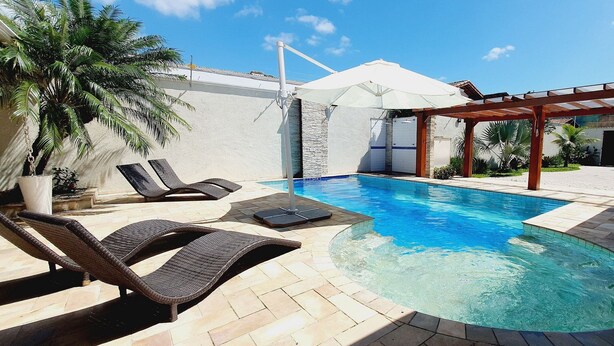 A swimming pool with lounge chairs and a pergola, surrounded by a landscaped garden and a building with a stone facade.