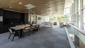 A modern conference room with a wooden ceiling, a large table with chairs, a foosball table, and large windows offering a view of the outdoors.
