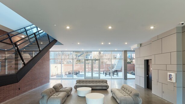 A spacious lobby with a high ceiling, a staircase, and a large seating area with modern sofas and round tables.