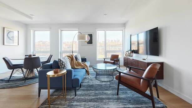 Un salon moderne avec un canapé, une table basse et des fauteuils, de grandes fenêtres et un téléviseur à écran plat.