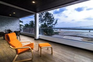 A balcony with wooden flooring, orange chairs, and a view of the beach.