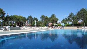 A swimming pool with lounge chairs and umbrellas, surrounded by trees. - Lovely Studio With 12 Shared Pools - Beahost (San Michele al Tagliamento)