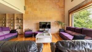 Ein modernes Wohnzimmer mit einem großen Flachbildfernseher, violetten Sofas, einem weißen Couchtisch und einer Steinwand.