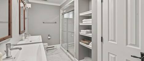 Un bagno moderno con due lavabi, box doccia in vetro e scaffali a muro con asciugamani.