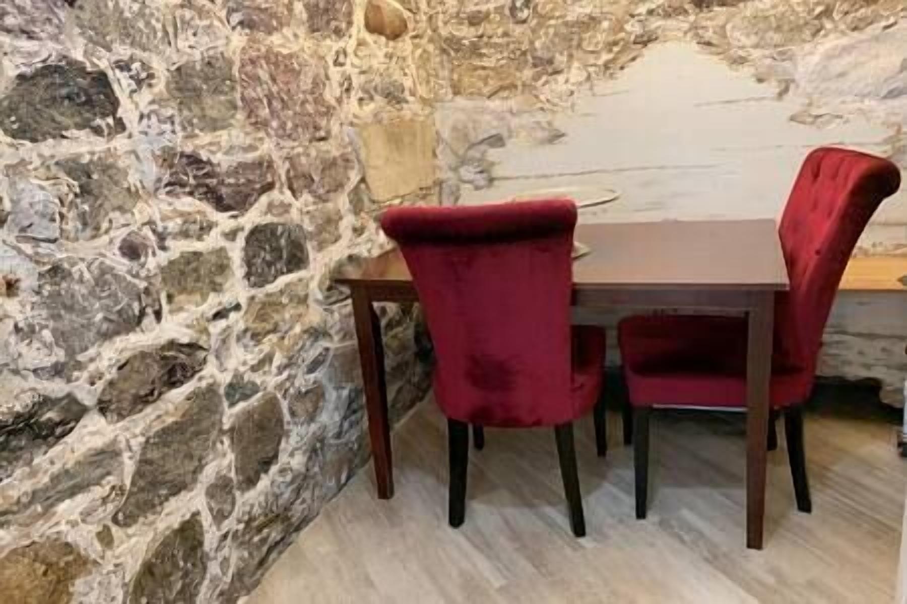 Un mur de pierres, une table en bois et deux chaises rouges.