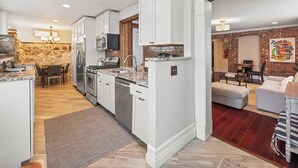 A modern kitchen with white cabinetry, a stone accent wall, and a dining area with a wooden table and chairs. - C&J Signature Stays Historic renovated apartment (Morristown)