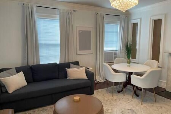 A modern living room with a dark sofa, a round coffee table, and a dining area with a white table and chairs.