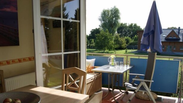 Eine Terrasse mit Tisch und Stühlen, eine Schüssel mit Äpfeln und Blick auf einen Garten und ein Haus.