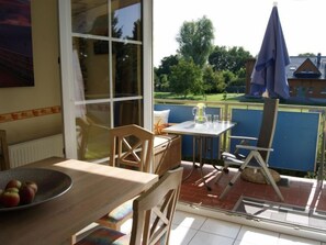Une terrasse avec une table et des chaises, un panier de pommes et une vue sur un jardin et une maison.