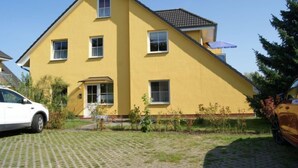 Ein gelbes, zweistöckiges Haus mit einem Ziegeldach, einer Veranda und einer Auffahrt.