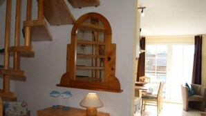 Eine Holztreppe, ein Holzkabinett mit einer Lampe und ein Essbereich mit Stühlen und einem Tisch.