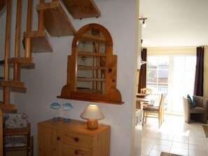 Uma escada de madeira, um armário de madeira com uma luminária e uma sala de jantar com cadeiras e uma mesa.