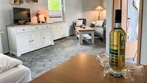 Ein gemütliches Wohnzimmer mit Fernseher, Couchtisch und einer Weinflasche auf einem Holztisch.