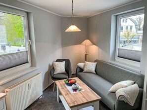 Et moderne og kompakt opholdsrum med en grå sofa, et træbord med skåle med frugt, en gulvlampe og en radiator.