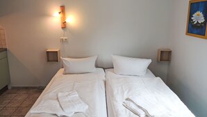 Ein Doppelzimmer mit zwei Betten, jeweils mit weißer Bettwäsche und Kissen, einem Nachttisch mit Lampe sowie einer kleinen Holzablage.