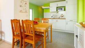Een moderne keuken met witte kasten en een groene accentmuur, een houten eettafel met stoelen, en een magnetron boven de kasten.
