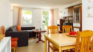 Een gezellige woonkamer met een bank, een eettafel met stoelen en een keuken met kasten en een raam.