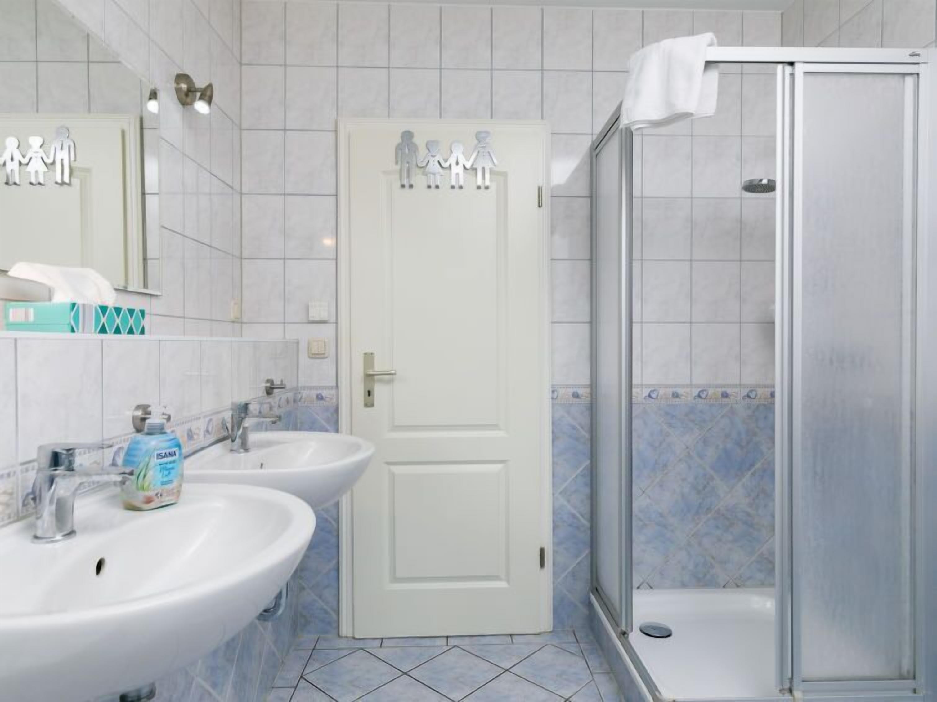 Een badkamer met twee wastafels, een douche en een deur met een decoratie van een gezinssilhouet.