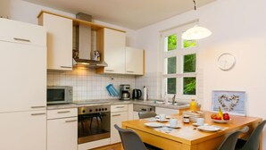 A modern kitchen with white cabinets, a wooden dining table, and a view of greenery outside. - Apartment Meise by Interhome (Zinnowitz)