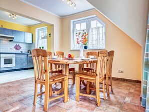 Un coin repas avec une table et des chaises en bois, une cuisine à l’arrière-plan et une fenêtre donnant sur un paysage.