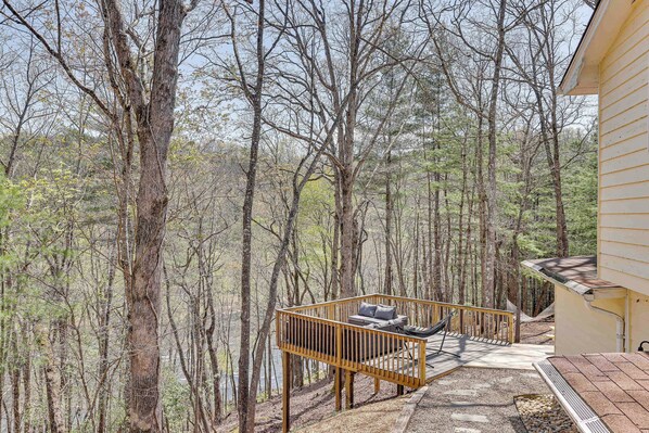 Relax on the serene deck surrounded by a dense forest, with a bench and table for a peaceful retreat.