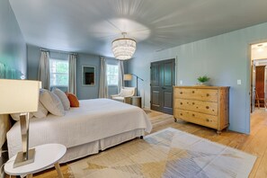 Cozy retreat with a large bed, dresser, and nightstand, featuring a chandelier and window with curtains.