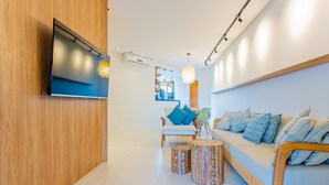Una sala de estar moderna con un televisor de pantalla plana montado en una pared de madera, un sofá con cojines estampados y una zona de comedor al fondo.