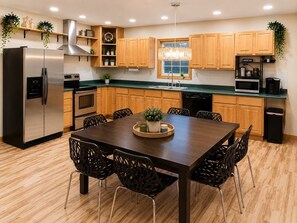 A modern kitchen with wooden cabinets, stainless steel appliances, and a dining area with a dark wooden table and chairs.