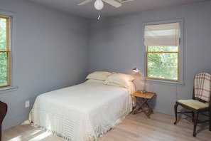 Quarto com cama, cadeira, mesa de cabeceira e ventoinha no teto.