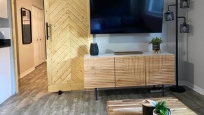 Ein modernes Wohnzimmer mit einer rautenförmigen Schiebetür, einem großen Flachbildfernseher, der an einer Holzkonsole befestigt ist, und einer Stehlampe mit schwarzem Metallgehäuse.