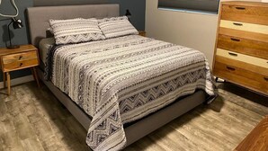 Ein Schlafzimmer mit einem Bett, Nachttischen, einer Kommode und einem Fenster mit Jalousien.