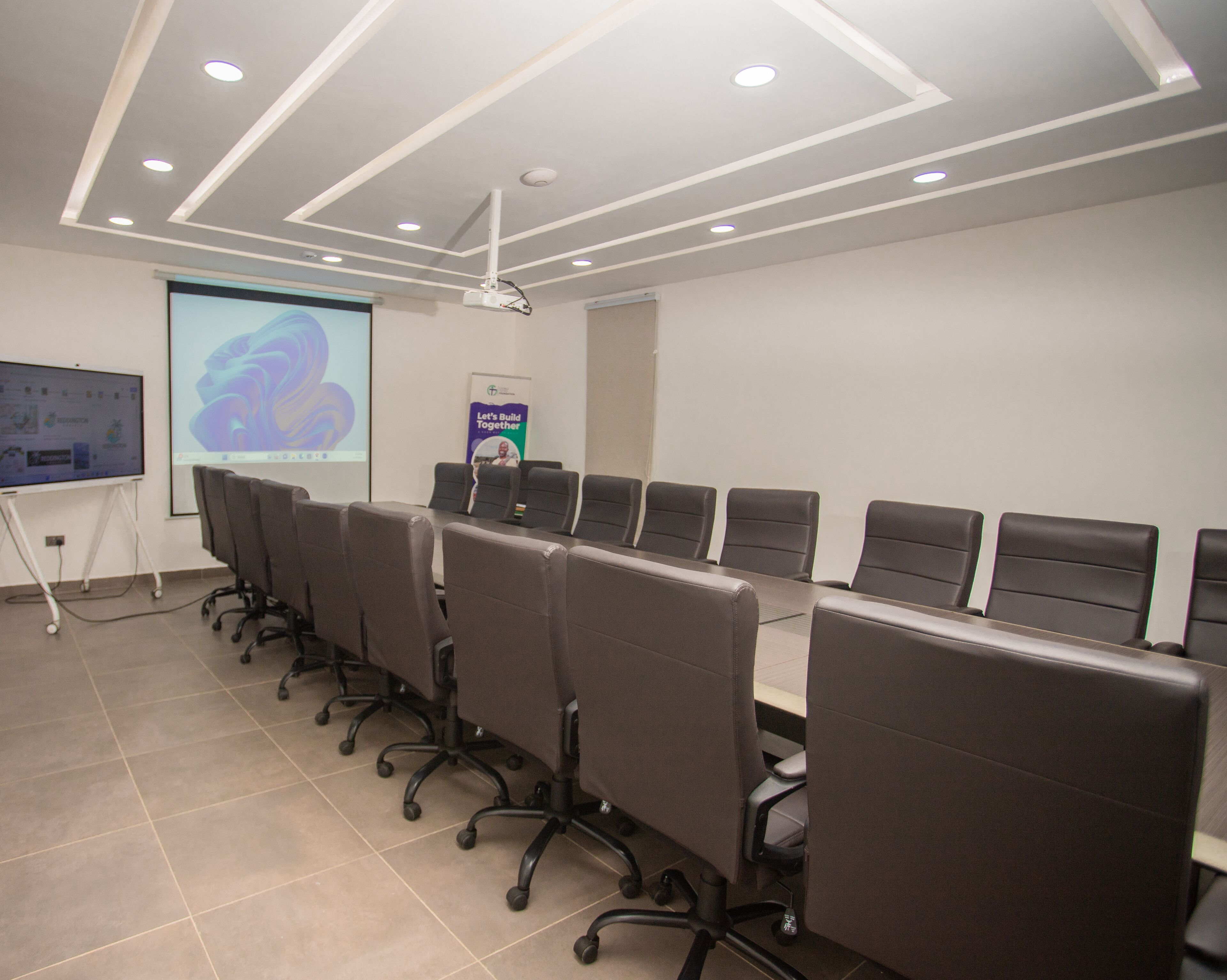 Un salón de conferencias con una larga mesa, varias sillas, una pantalla de proyector y una pantalla para presentaciones.
