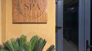 A wooden plaque with "The Spa" and "Reddington" on a wall, a door with a handle, and green plants at the base. - Reddington Beach Resort (Anloga)
