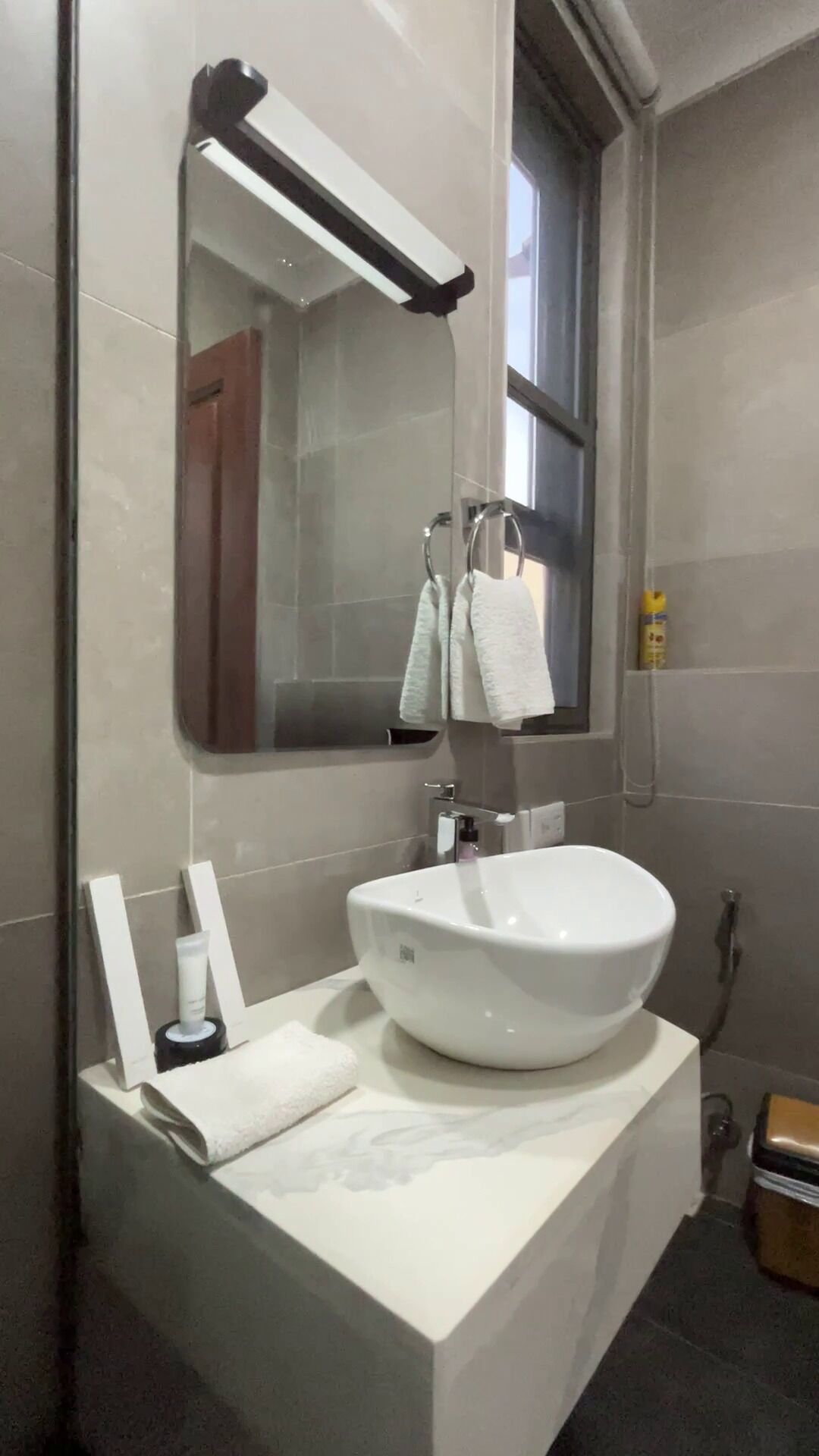 A modern bathroom with a white sink, a large mirror, and a towel rack.