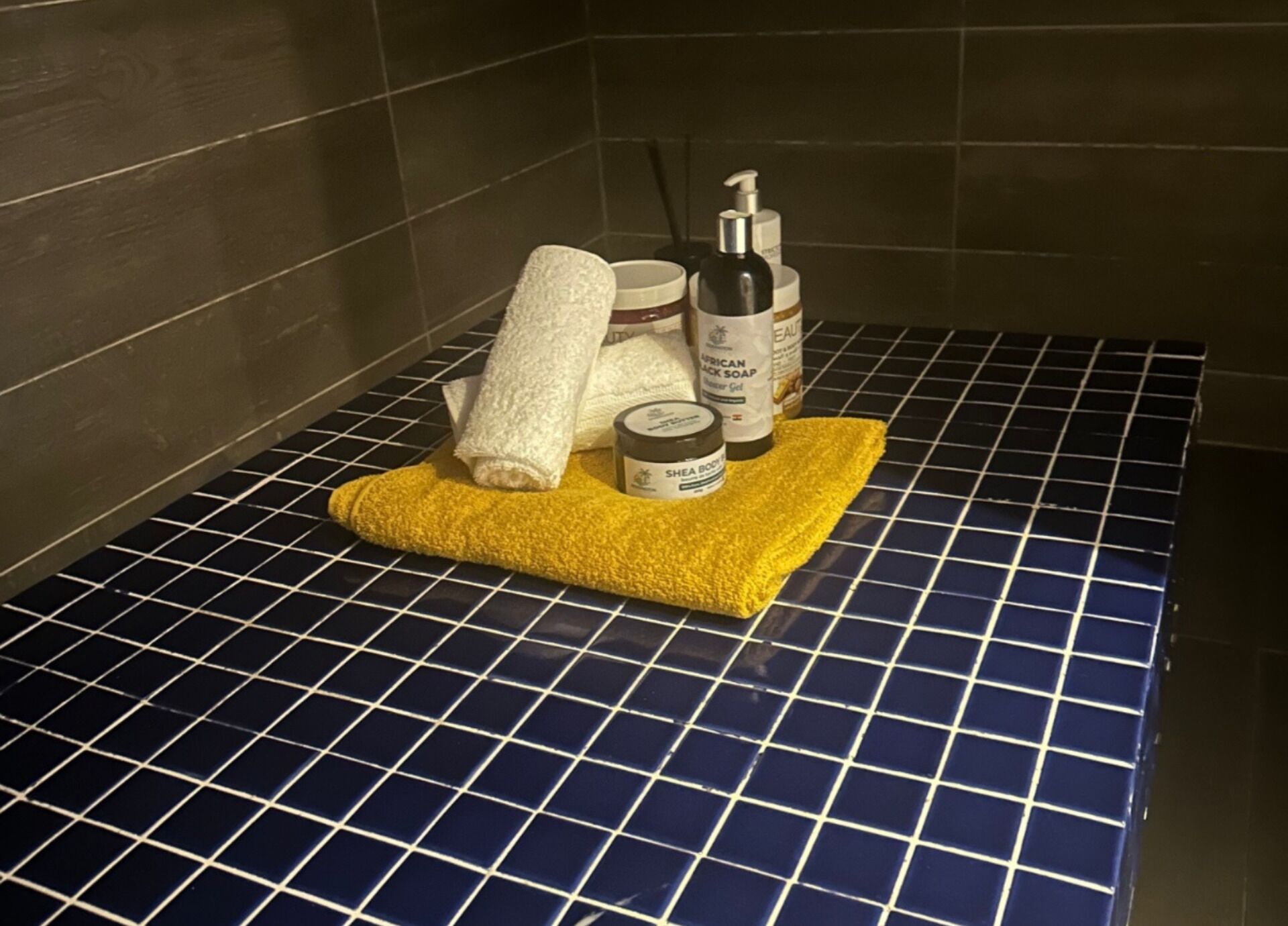 A bathroom with a blue-tiled floor, a yellow towel, a white towel, and two bottles of soap.