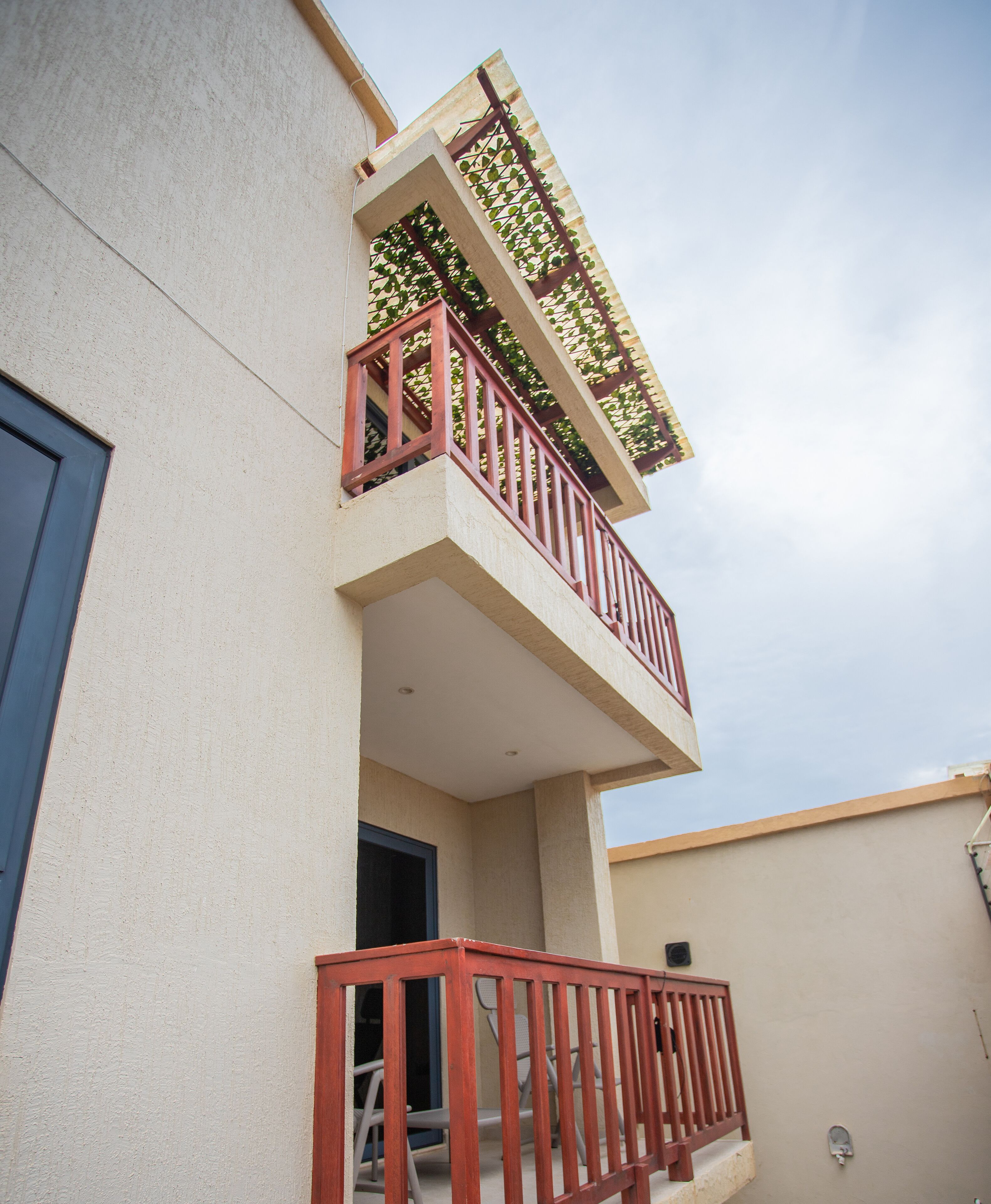 A building with a balcony featuring a red railing and a small enclosed area with a chair.