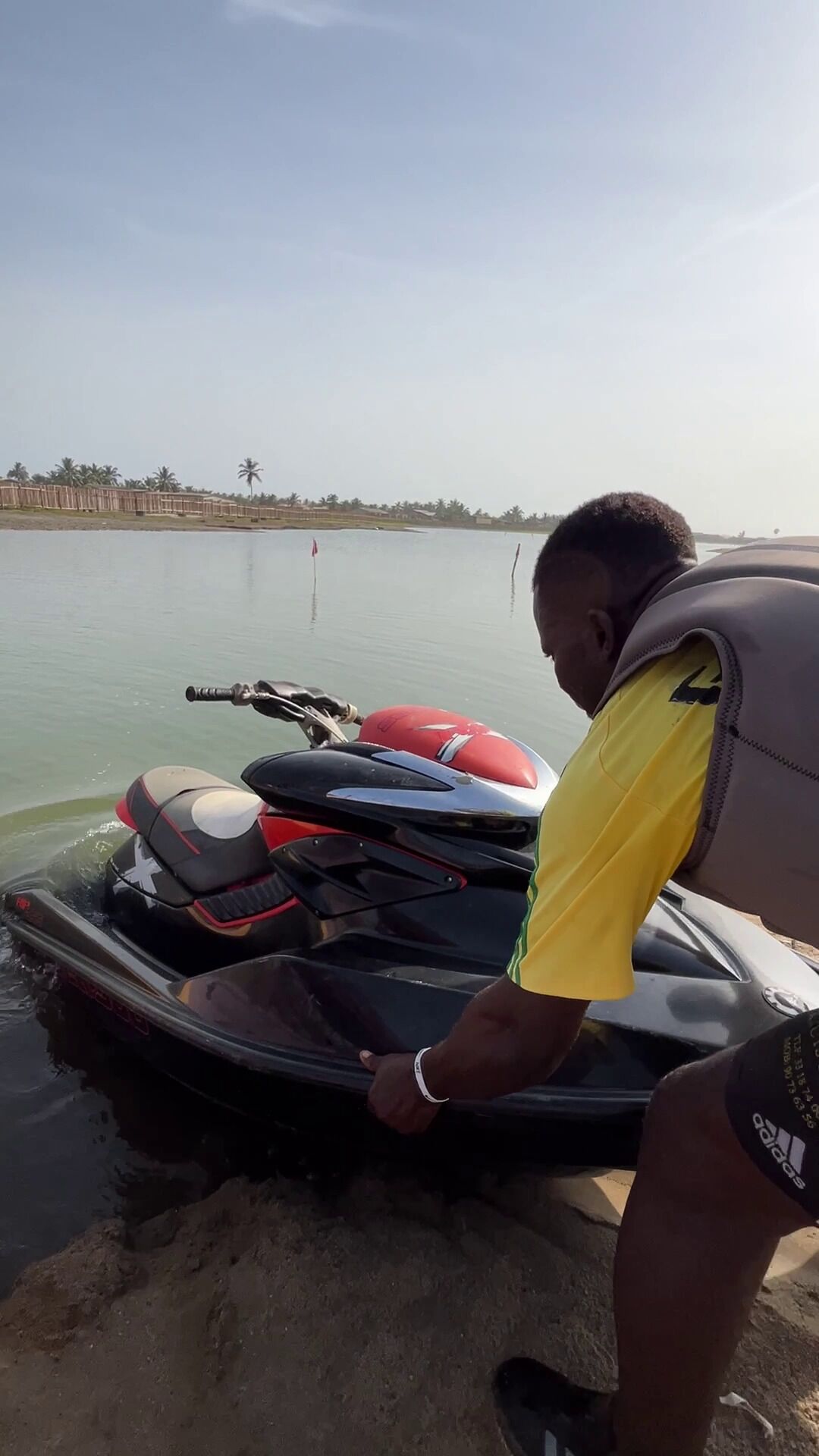 A person preparing a jet ski on a calm body of water with a distant shoreline and palm trees.